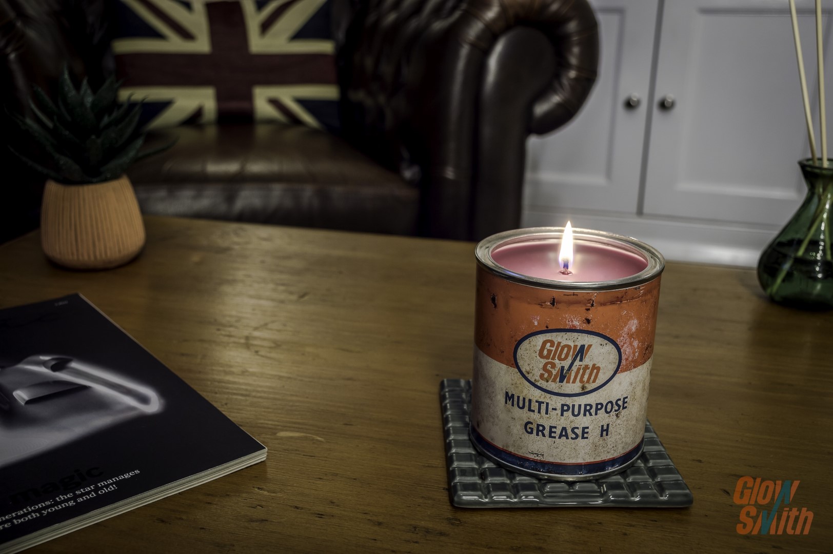 Glowsmith container candle burning on wooden table in a man cave with leather sofa in background